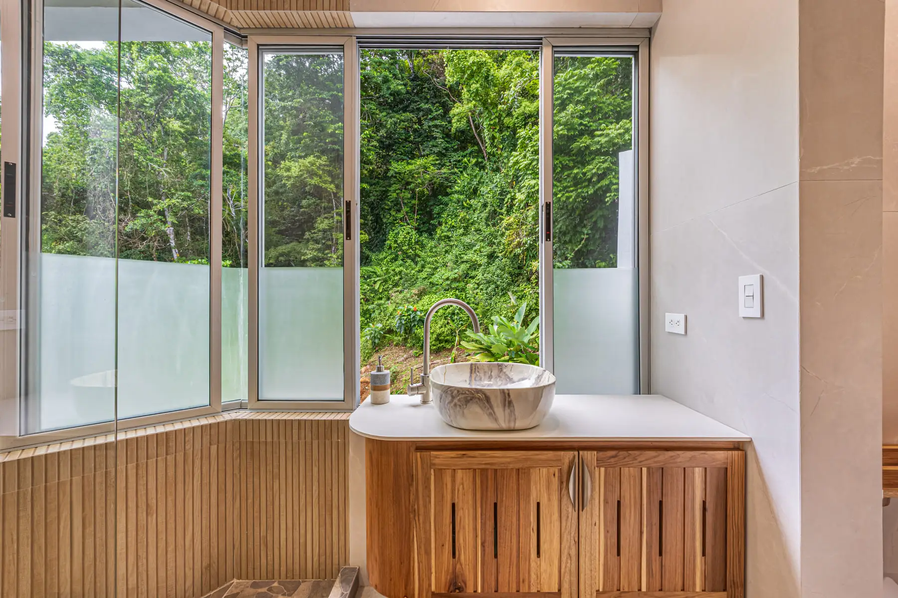A carved stone basin on a hardwood vanity, with a window straight into the greenery
