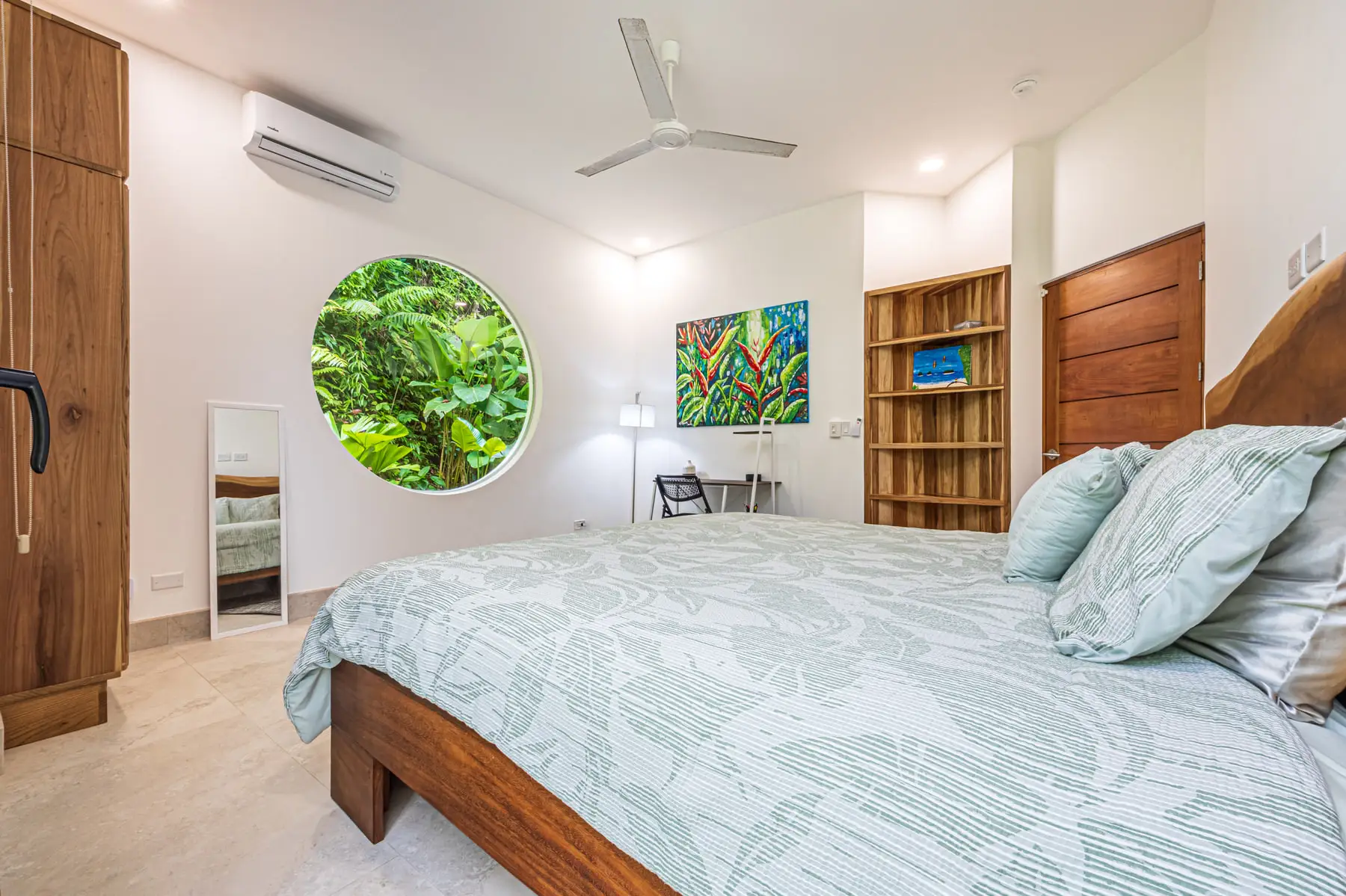 A queen bedroom with a round window framing the forest