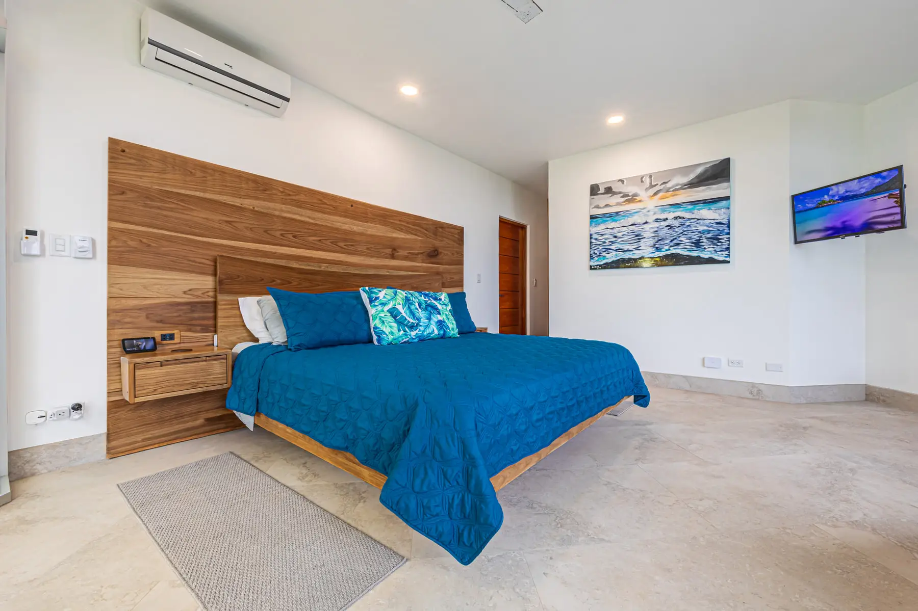 A king bedroom with a hardwood headboard and a painting of the coast