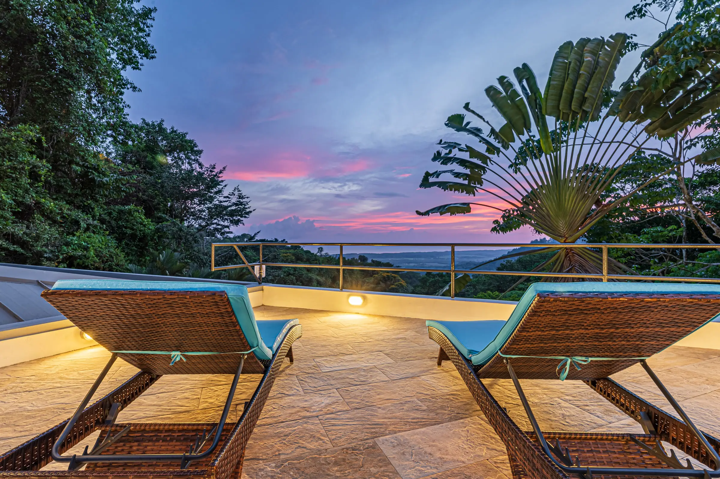 Two loungers on the stone deck facing the Pacific horizon at sunset