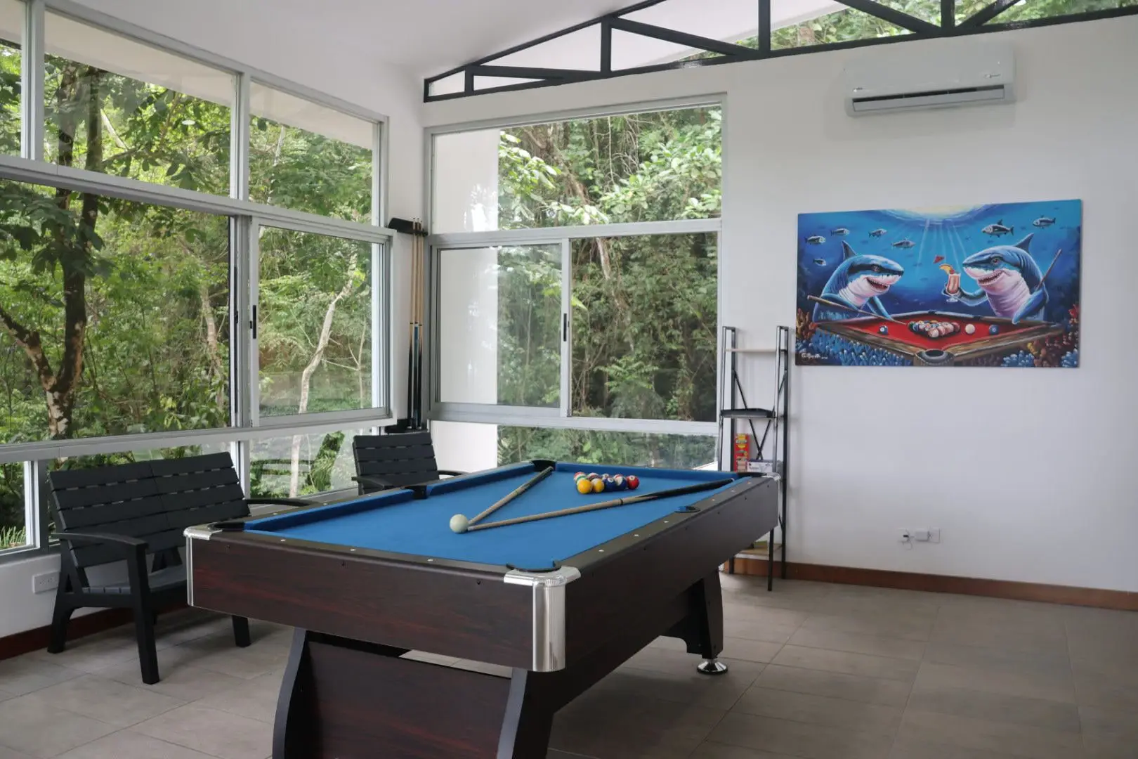 The game room, a full-size pool table under tall windows onto the forest
