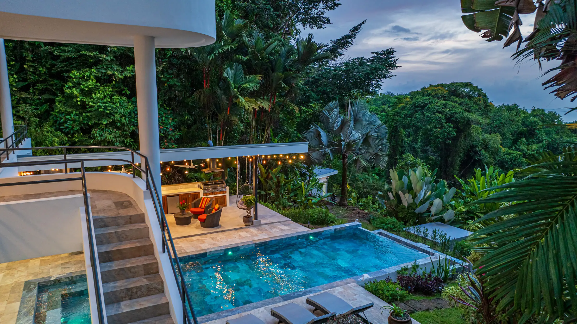 The house and pool from the air at dusk, lights on under the covered terrace