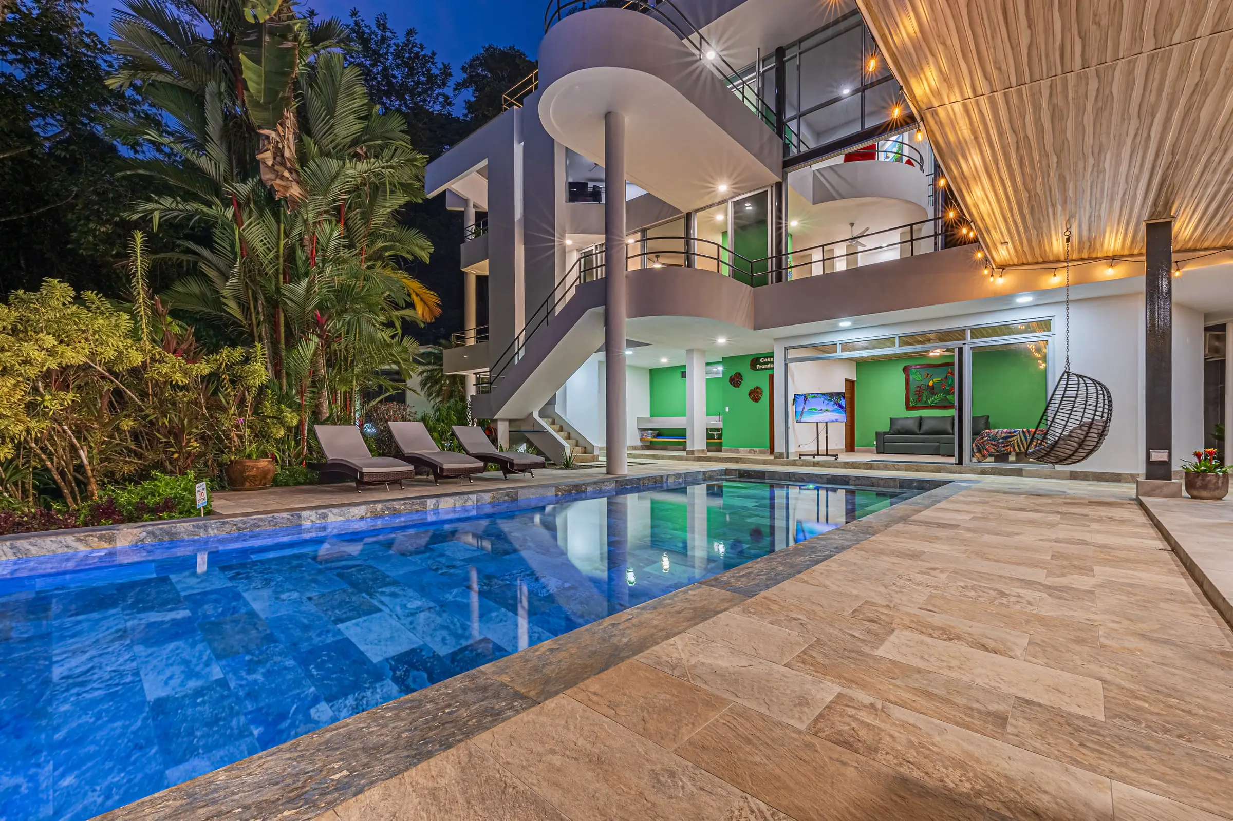 The house lit from within after dark, reflected in the pool