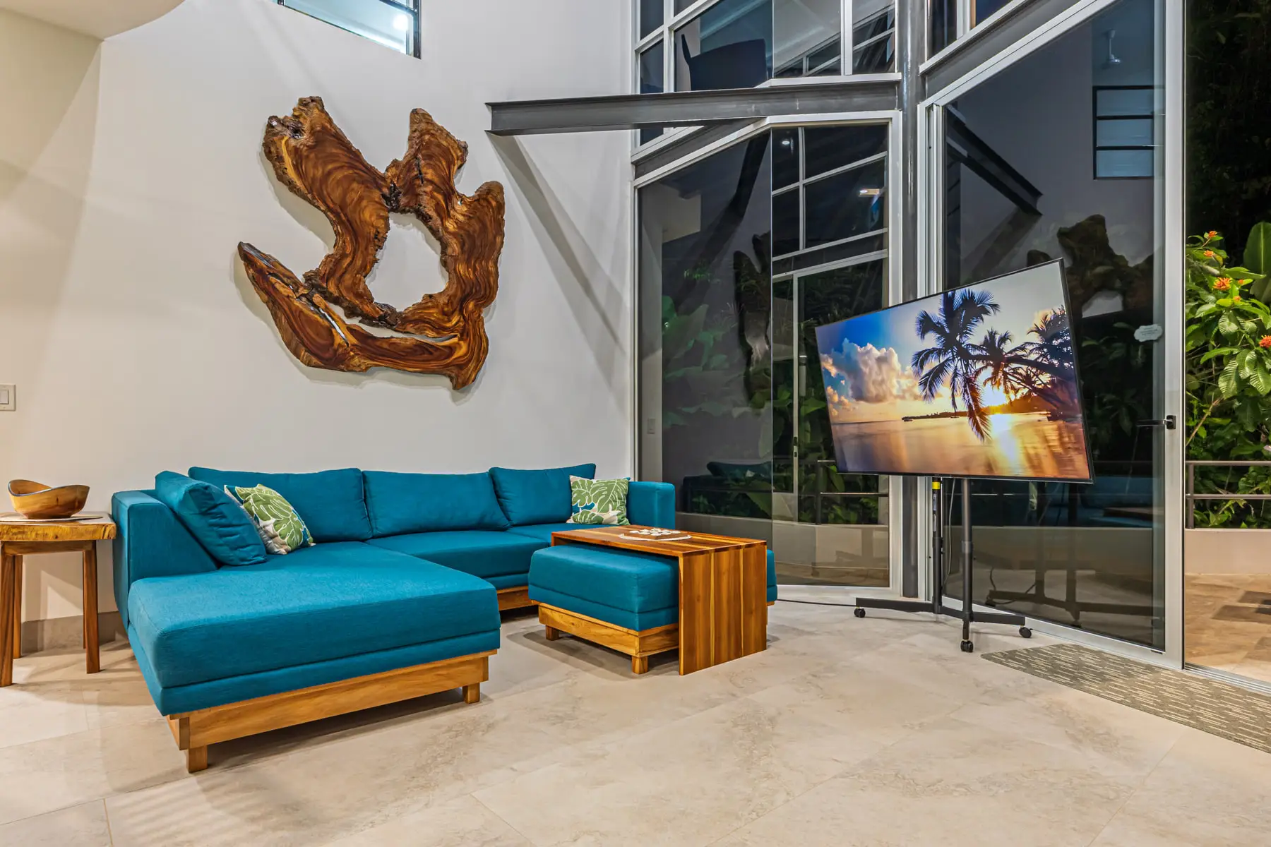 The living room, a teal sectional facing a double-height glass wall onto the jungle