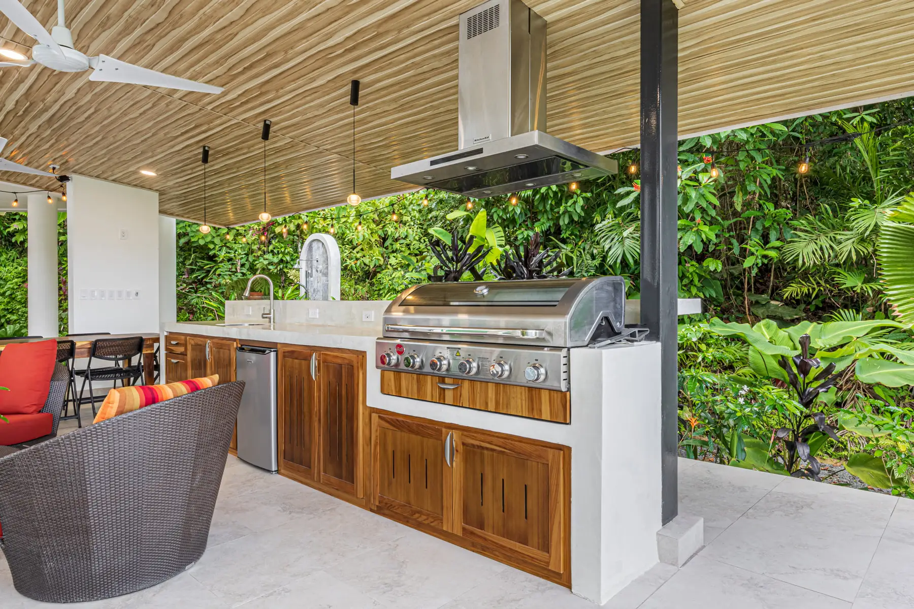 The outdoor kitchen with a gas grill, sink and hardwood cabinets, open to the jungle