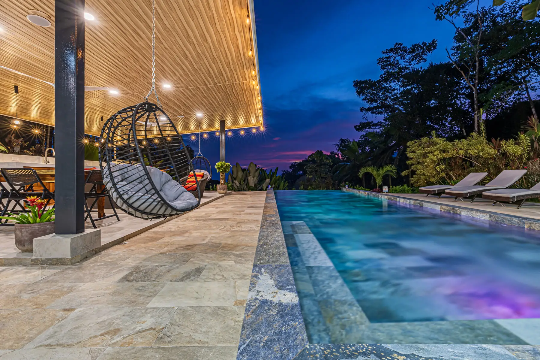 A hanging chair beside the lit pool after dark, under strings of warm light